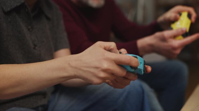 Close-up of mature couple pressing gamepads buttons, immersed in a video game