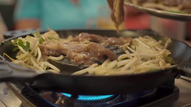Sizzling slices of marinated lamb and fresh bean sprouts cooking on a special convex metal skillet over a gas burner, a popular grilled mutton dish from Hokkaido, Japan called jingisukan