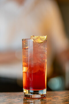 View of a refreshing red cocktail in a tall glass filled with ice and garnished with a lime wedge on a bar counter in Asker, Akershus, Norway.