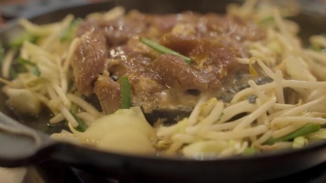 Close up of traditional Japanese jingisukan barbecue with lamb and vegetables cooking on a cast iron skillet. Hot steam rises from the sizzling mutton and bean sprouts in a Hokkaido restaurant