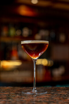 View of an espresso martini cocktail served in a stemmed glass on a polished bar counter in a dimly lit bar in Asker, Akershus, Norway.