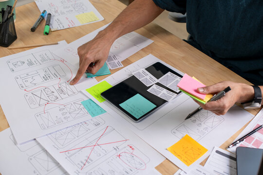 UX UI designer working on wireframes for a website and mobile app prototype, surrounded by sketches of user-flow and design tools, in concept of website and mobile application design concept.