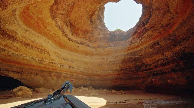 View from a tour boat entering the famous Benagil Cave with a sandy beach, layered limestone walls and natural skylight in Portugal.