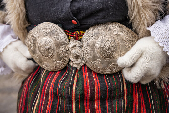 Woman in traditional clothing with large brass belt at a Kukeri festival in Bulgaria.