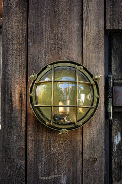 Round brass industrial wall lamp on weathered wooden boards.