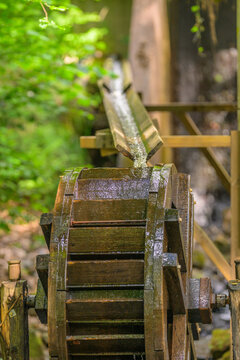 Water channel feeding historic wooden mill wheel in leafy forest.