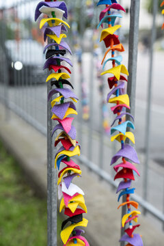 Colorful felt decorations hanging on metal fence in city.