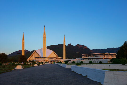View of Faisal Masjid with its distinctive minarets and tent-like structure set against the backdrop of the Margalla Hills under a clear blue sky in Islamabad, Islamabad Capital Ter, Pakistan.