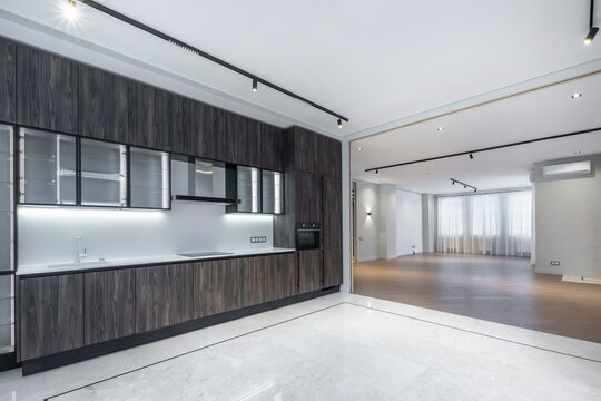 A new apartment showcases a modern kitchen with sleek designs and a spacious living area. Large windows allow natural light to fill the space. The flooring is light in color