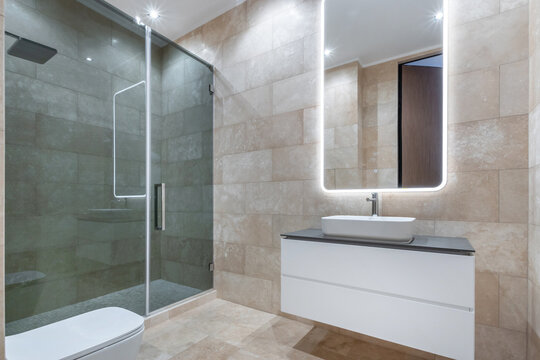 A clean bathroom shows a glass shower with tiles and a modern sink. Bright lights highlight the mirror. This room is part of a contemporary home
