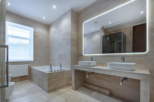 A spacious bathroom features a large bathtub and two sinks with sleek mirrors. Soft lighting highlights the clean lines and simple design in this bright room