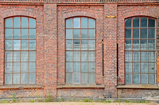 Historic brick industrial facade with tall arched factory windows, weathered masonry, repeating symmetry, aged glass panes, urban architectural texture and vintage warehouse character