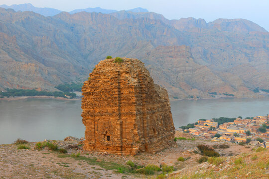 View of the ancient Mari Indus Temple from the Hindu Shahi period standing on a cliff overlooking the Indus River with rugged mountains and a town in the background in Kalabagh, Punjab, Pakistan.