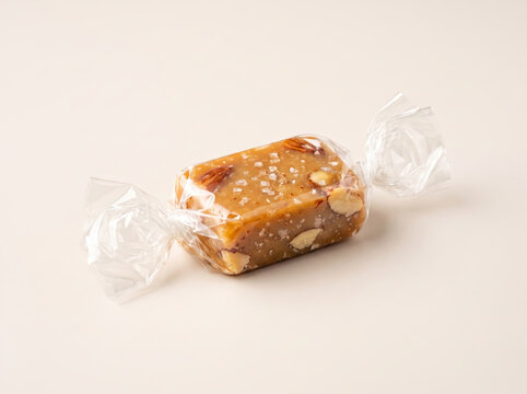 Salted caramel candy with almonds wrapped in clear plastic on a light surface