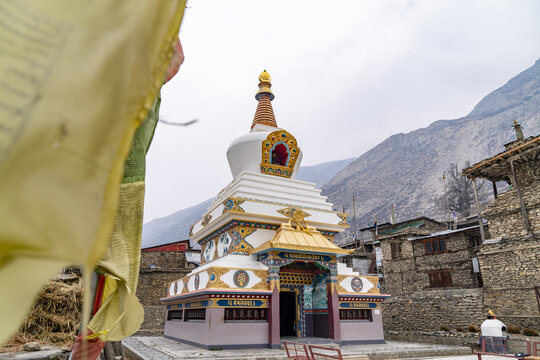 View of the Tanki Manang stupa with its ornate golden roof and colorful details, set against rugged stone buildings and mountain landscape in Manang, Gandaki Province, Nepal.