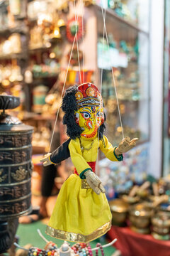 View of a traditional Nepali marionette puppet hanging in a shop on Thamel Marg, featuring a yellow dress and ornate mask, surrounded by crafts in Kathmandu, Bagmati Province, Nepal.