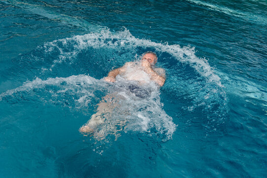 Man swimming in a pool during a sunny day while creating splashes of water
