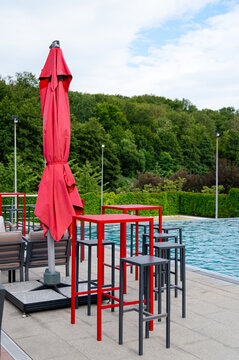 Red patio furniture near a swimming pool surrounded by green trees in the daytime