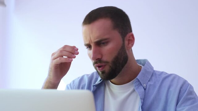 Overworked male professional feeling stressed while working on his laptop in the office, suffering from a severe headache, burnout, and mental fatigue from overwhelming tasks and deadlines