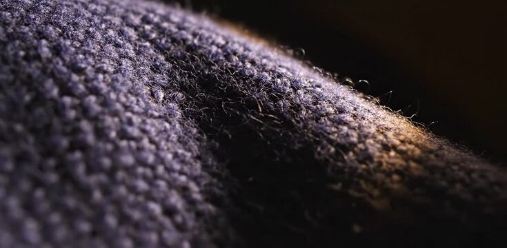 Close up macro view of a deep purple knit fabric showing intricate wool texture with warm golden highlights