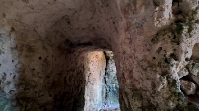 Xemxija, Malta 29.07.2026 - Heritage trail, Roman Baths, shelf like cut in the stone Dark cave walls show rough, textured surfaces. Greenish moss grows on damp, uneven stone. Light filters through nar