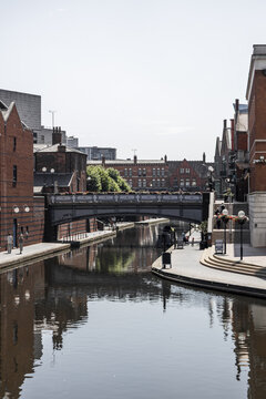 View of the historic canal network in Birmingham, featuring a metal bridge, red brick buildings, and a calm waterway reflecting the architecture in Birmingham, England, United Kingdom.