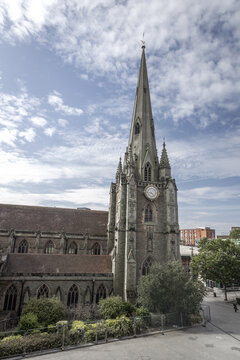 View of St Martin in the Bull Ring church with its tall spire, stone architecture, and clock face, set against a blue sky with clouds in Birmingham, England, United Kingdom.