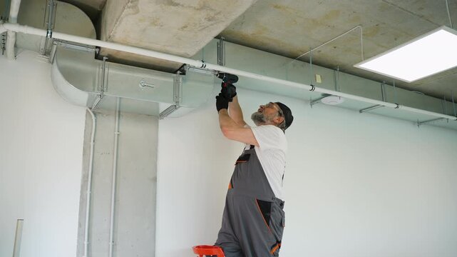 Older handyman installing ventilation system with cordless screwdriver
