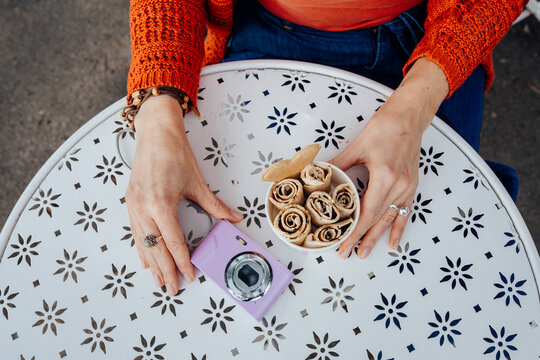 Overhead view of woman arranging rolled ice cream and compact camera on cafe table
