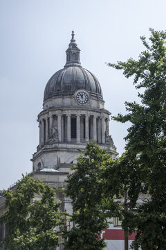 View of the neoclassical dome and clock tower of the Nottingham Council House surrounded by lush green trees in Nottingham, England, United Kingdom.