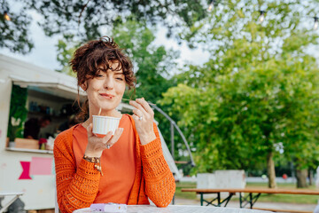 Fototapeta premium Playful middle-aged woman tasting rolled ice cream at outdoor cafe with copy space