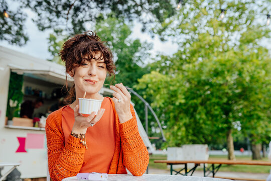 Playful middle-aged woman tasting rolled ice cream at outdoor cafe with copy space