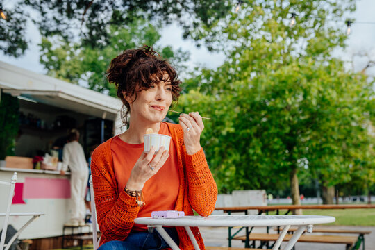 Relaxed middle-aged woman enjoying rolled ice cream at outdoor cafe with copy space