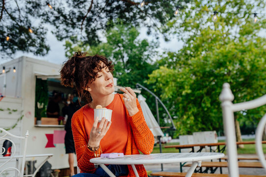 Relaxed middle-aged woman savoring rolled ice cream at outdoor cafe with copy space