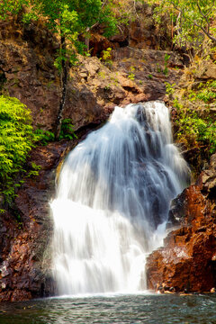 People enjoy swimming in the refreshing pool at the base of a scenic tropical waterfall. The cascading water falls over ancient rugged rocks and green vegetation.