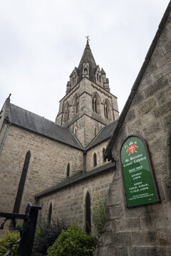 View of the historic stone architecture of St. Barnabas Catholic Cathedral with its tall spire and a mass times sign in Nottingham, England, United Kingdom.