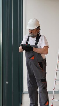 Senior construction worker drilling window frame with cordless screwdriver