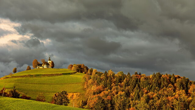 Sorrowful Mother of God church (Cerkev Zalostne Matere Bozje) on a hilltop, lit by the sun in an otherwise cloudy autumn dawn. Bukov Vrh-Slovenia-187