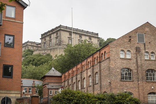 View of Nottingham Castle perched on a sandstone cliff above historic red brick buildings and lush trees in Nottingham, England, United Kingdom.