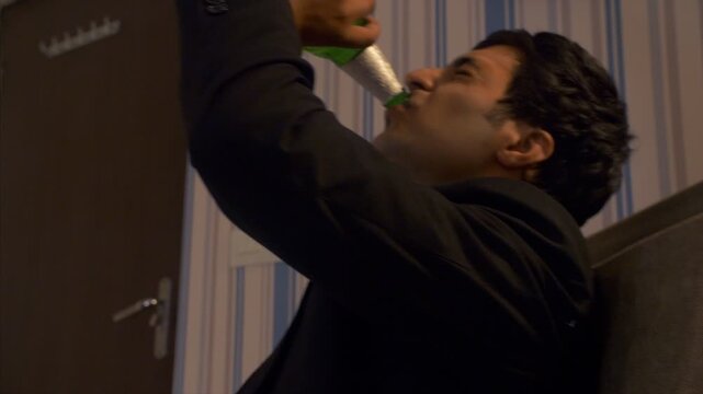 Upset Indian man drinking alcohol at home - depression  alcohol abuse  addiction  frustrated alcoholic . Young Asian employee relieving stress with a beer - work pressure  depressive thoughts  poor...