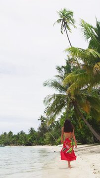 Vacation travel woman relaxing on paradise beach with palm trees on holidays. Girl on beach in pareo and bikini on Tahiti, French Polynesia. Vertical video of real woman model without any makeup
