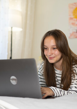 Teenage girl using laptop at home while relaxing in cozy bedroom 