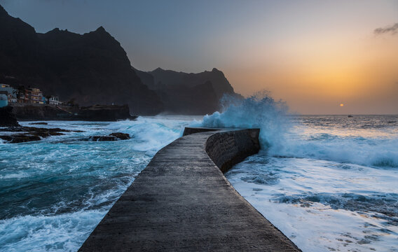 View of the stone pier at Santo Antao with waves crashing against the breakwater at sunset in Ponta do Sol, Ribeira Grande, Cabo Verde.