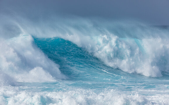 View of a powerful turquoise ocean wave breaking with sea spray and foam near the coast of Santo Antao, Ponta do Sol, Ribeira Grande, Cabo Verde.