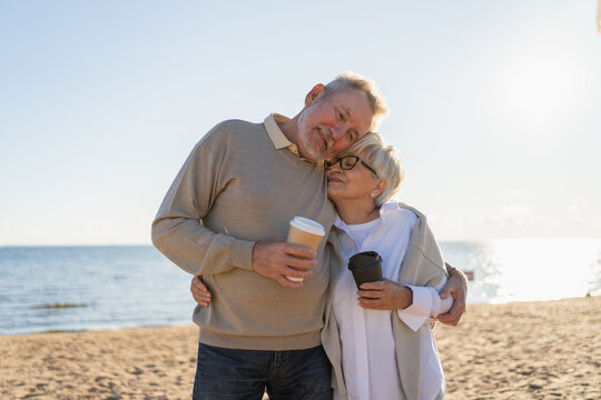 Good morning. Senior mature couple enjoying walking with paper cups of coffee. Old husband wife drinking coffee to go outdoor. Grandmother grandfather together enjoying walk. Family moment of love