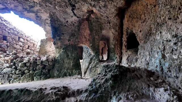 Xemxija, Malta 29.07.2026 - Heritage trail, Roman Baths, shelf like cut in the stone Dark cave walls show rough, textured surfaces. Greenish moss grows on damp, uneven stone. Light filters through nar