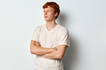 Young man with red hair and folded arms looking away in casual white t shirt against plain white background. Profile portrait of confident male model with freckles. © SHOTPRIME STUDIO