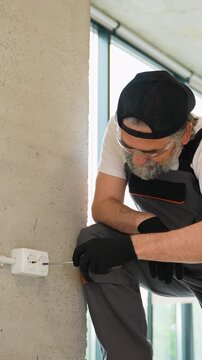 Professional electrician installing a wall socket with a screwdriver