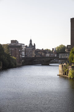 View of the River Ouse flowing through the historic city of York, featuring stone bridges and traditional brick architecture under a clear sky York, England, United Kingdom.