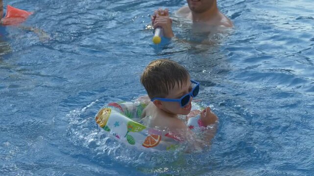 Two brothers and their father enjoy playful water fight with colorful water blasters in swimming pool. Childhood memories, laughter and carefree summer adventure concept.
